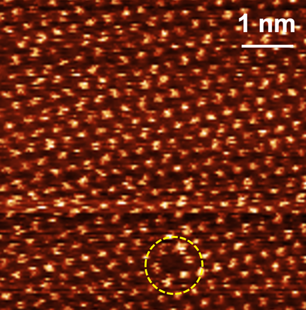 An atomic-resolution image of MoS2 acquired by Baykara Lab researchers, where bright dots represent individual sulfur atoms and a missing sulfur atom is highlighted by the dashed circle.